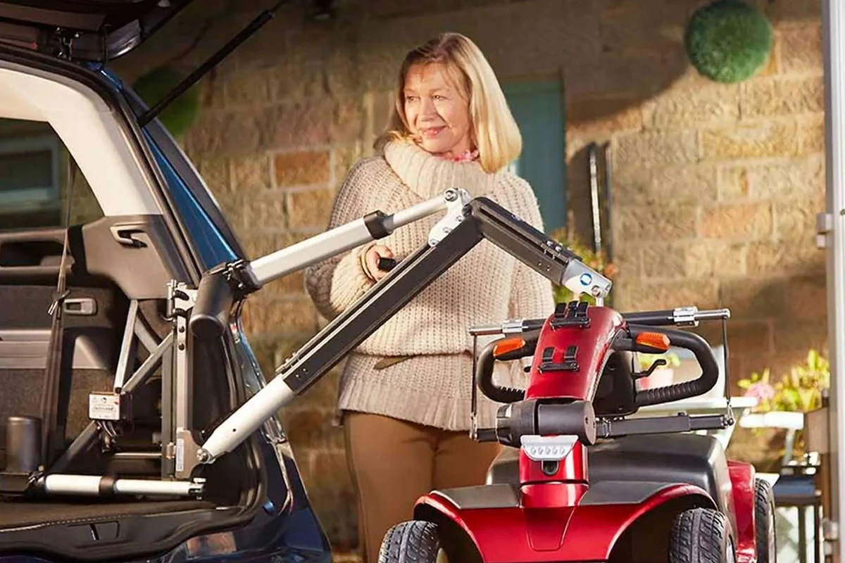 A woman using an Autochair boot hoist to lift a red mobility scooter